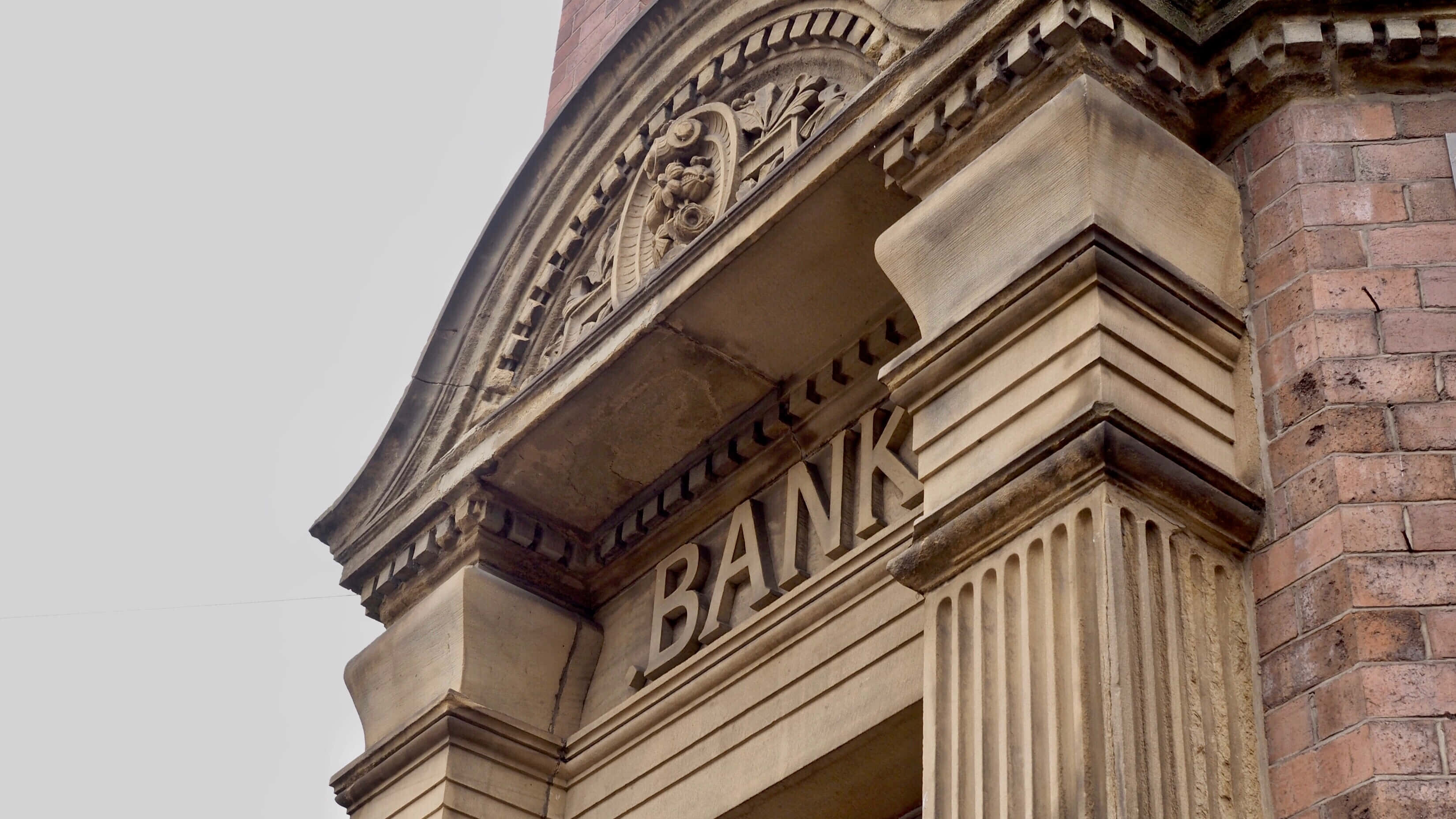 Bank 桌布 壁紙 — 歷史銀行建築華麗石砌外牆的特寫，帶有雕刻細節和粗體字，天空多雲。