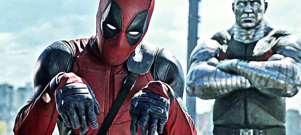 Deadpool And Colossus 桌布 壁紙 — 死侍身穿紅黑戰衣，自信地交叉雙臂，站在一個肌肉發達、身穿銀色盔甲的角色旁邊，背景是城市天際線。