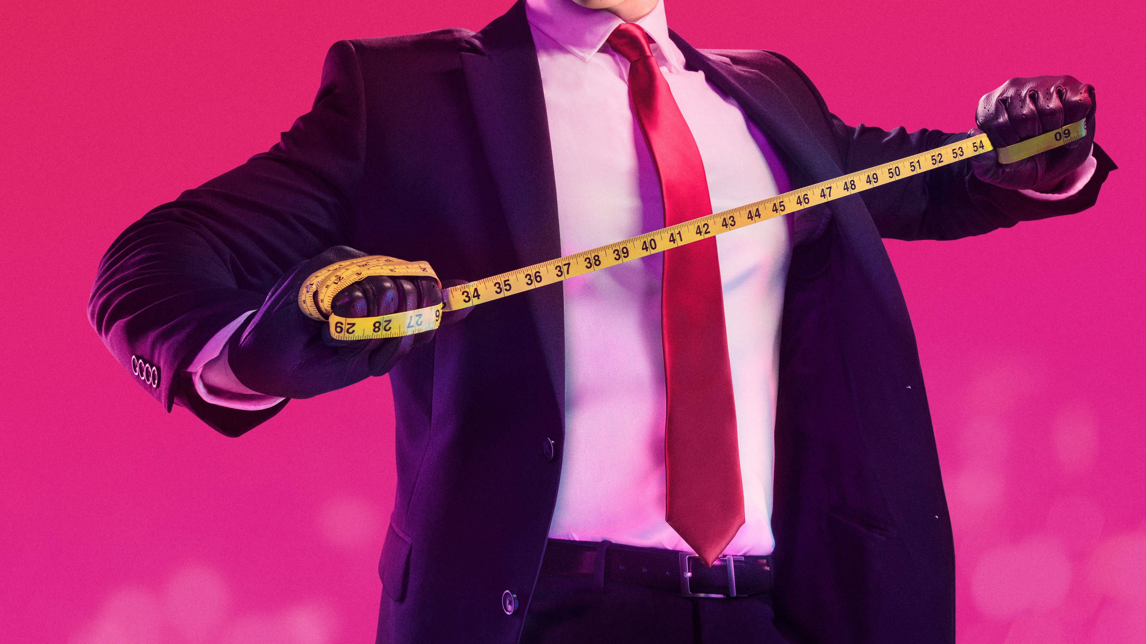殺手47 全4K 測量捲尺 壁紙 — 一位身穿西裝和紅色領帶的商人，在充滿活力的粉紅色背景前，將捲尺橫放在胸前。