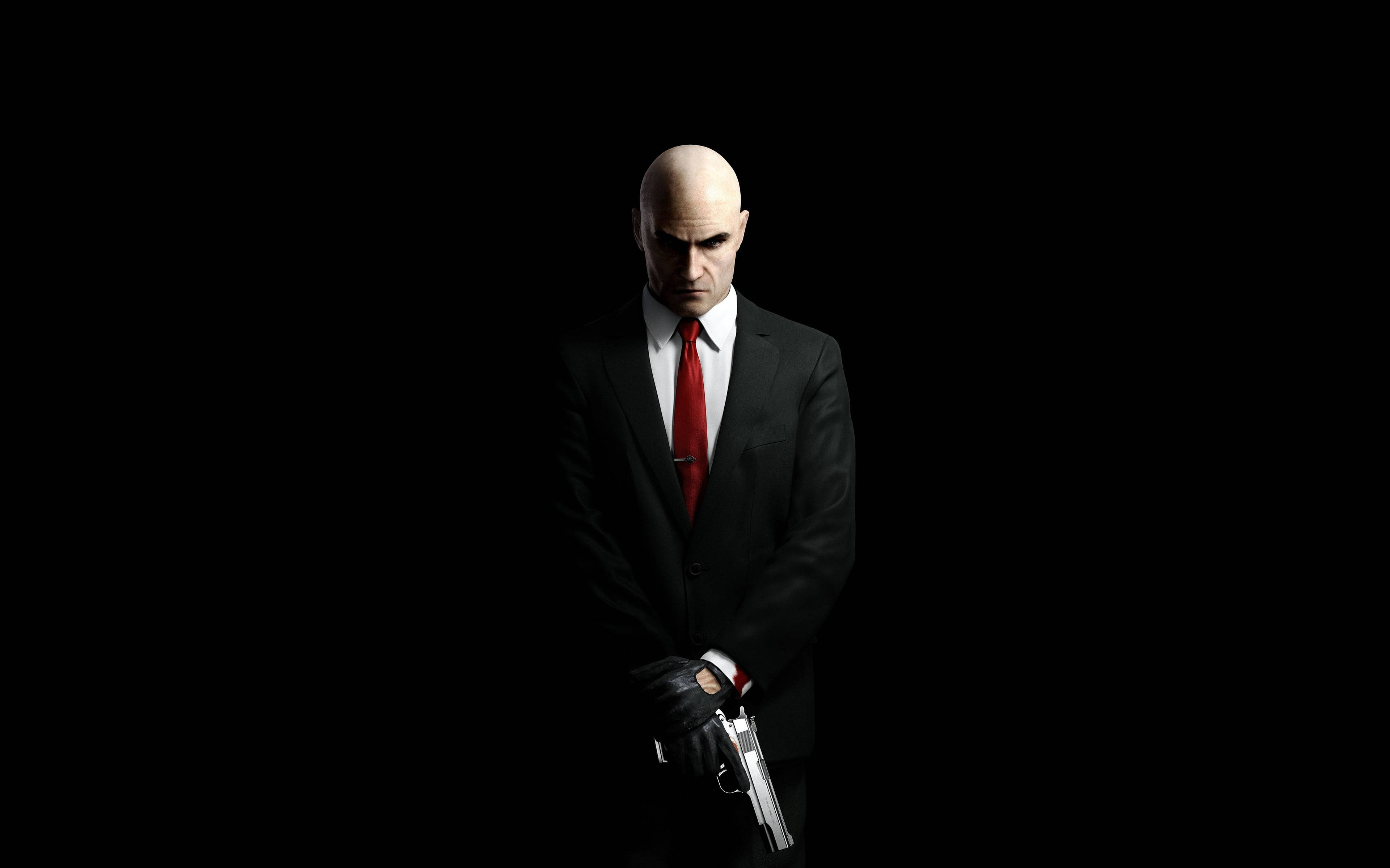 殺手47 全4K 西裝與手槍 壁紙 — 一個光頭男人穿著黑色西裝和紅色領帶，在純黑色背景前拿著一把銀色手槍。