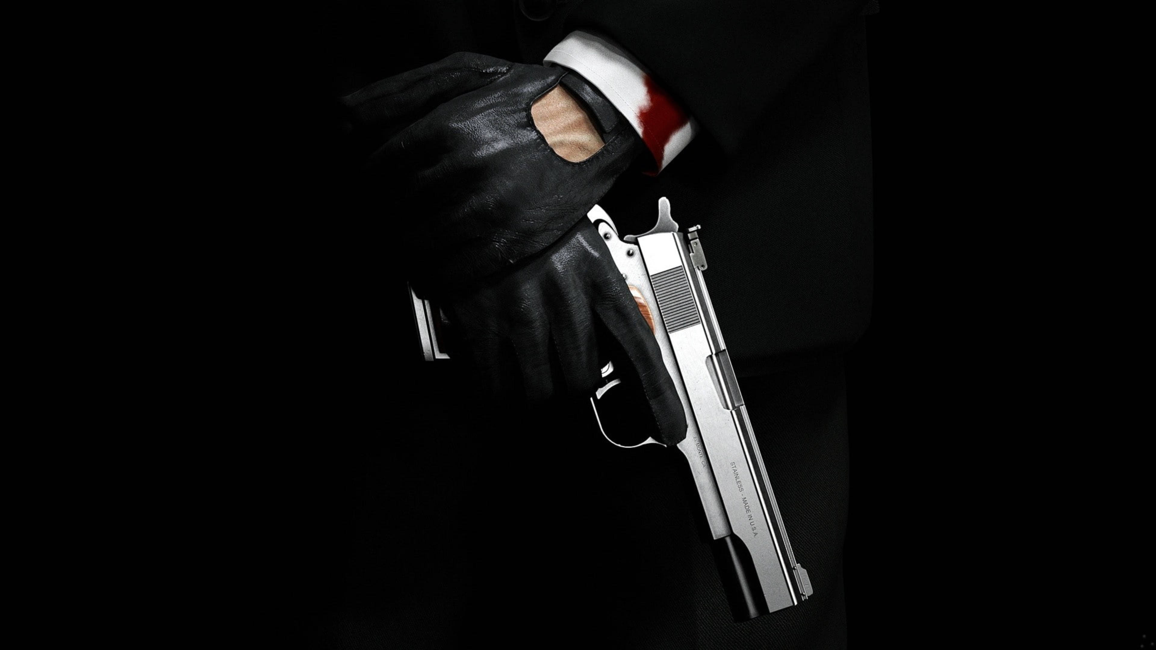 殺手47 全4K 銀色手槍 壁紙 — 一隻戴手套的手在黑色背景上握著一把銀色手槍，袖口沾有血跡。
