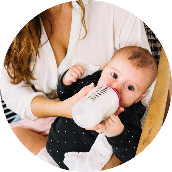 母親餵奶嬰兒 壁紙 — 一個穿著黑色圓點連身衣的嬰兒，由一位身穿白色襯衫的女性拿著白色奶瓶餵奶的特寫。