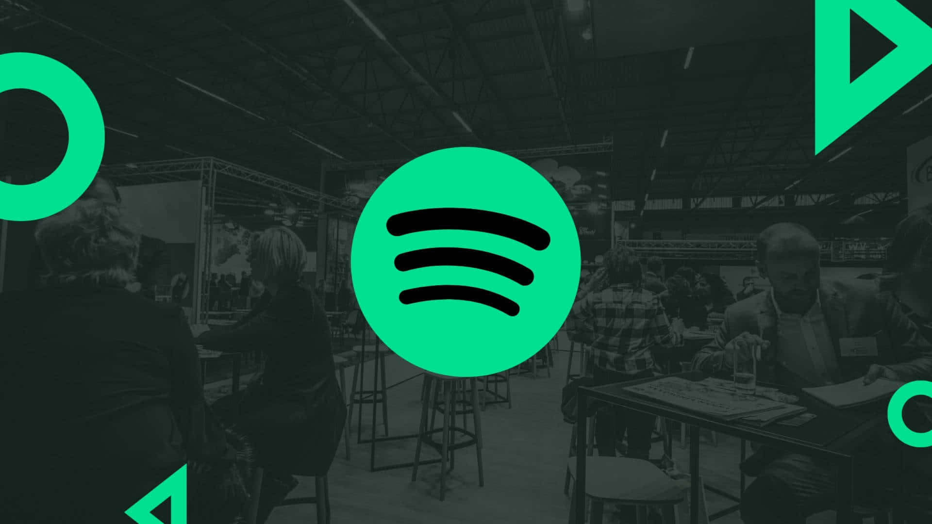 每一刻都有音樂相伴 - Spotify 壁紙 — 鮮綠色Spotify標誌疊加在燈光昏暗的會議廳，與會者在展位前。