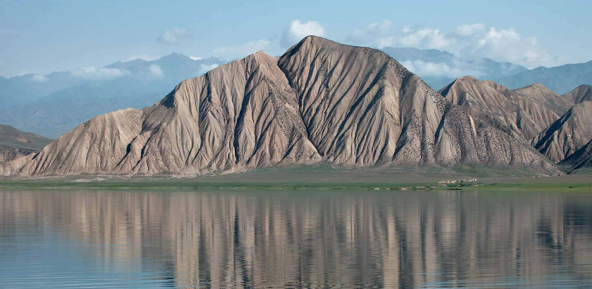 藍天白雲下，平靜湖面倒映著崎嶇山脈。