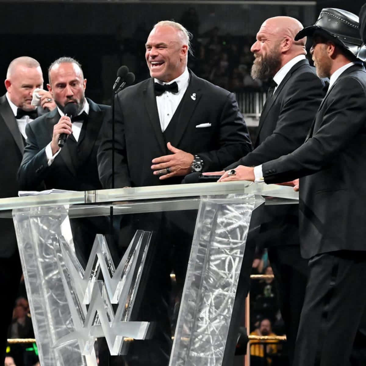 比利·岡恩參與D-Generation X WWE慶祝活動 壁紙 — WWE摔角手穿著禮服，在正式活動中笑著站在一個帶有WWE標誌的透明講台周圍。
