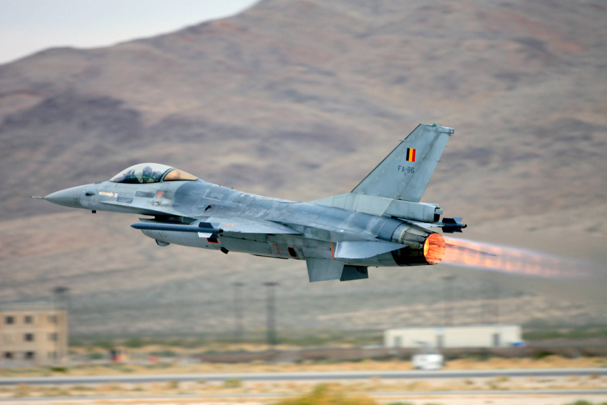 比利時空軍戰鬥機 壁紙 — 一架帶有比利時標誌的灰色戰鬥機在乾燥的山丘和跑道上，以熾熱的後燃器起飛。