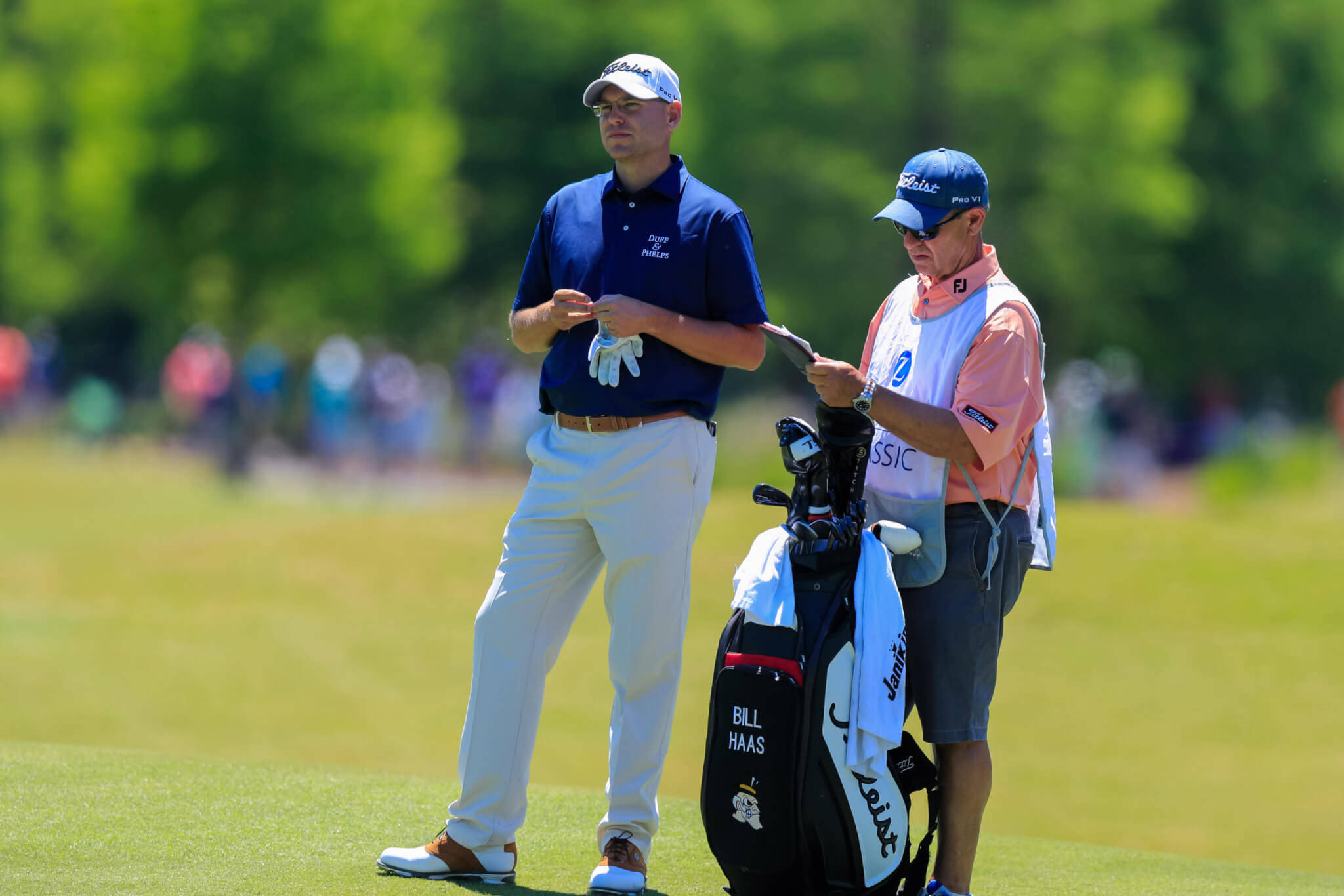 比爾·哈斯與他的球僮 壁紙 — 高爾夫球手 Bill Haas 和他的球童站在陽光普照的球道上，中間放著一個高爾夫球袋，正在檢討策略。