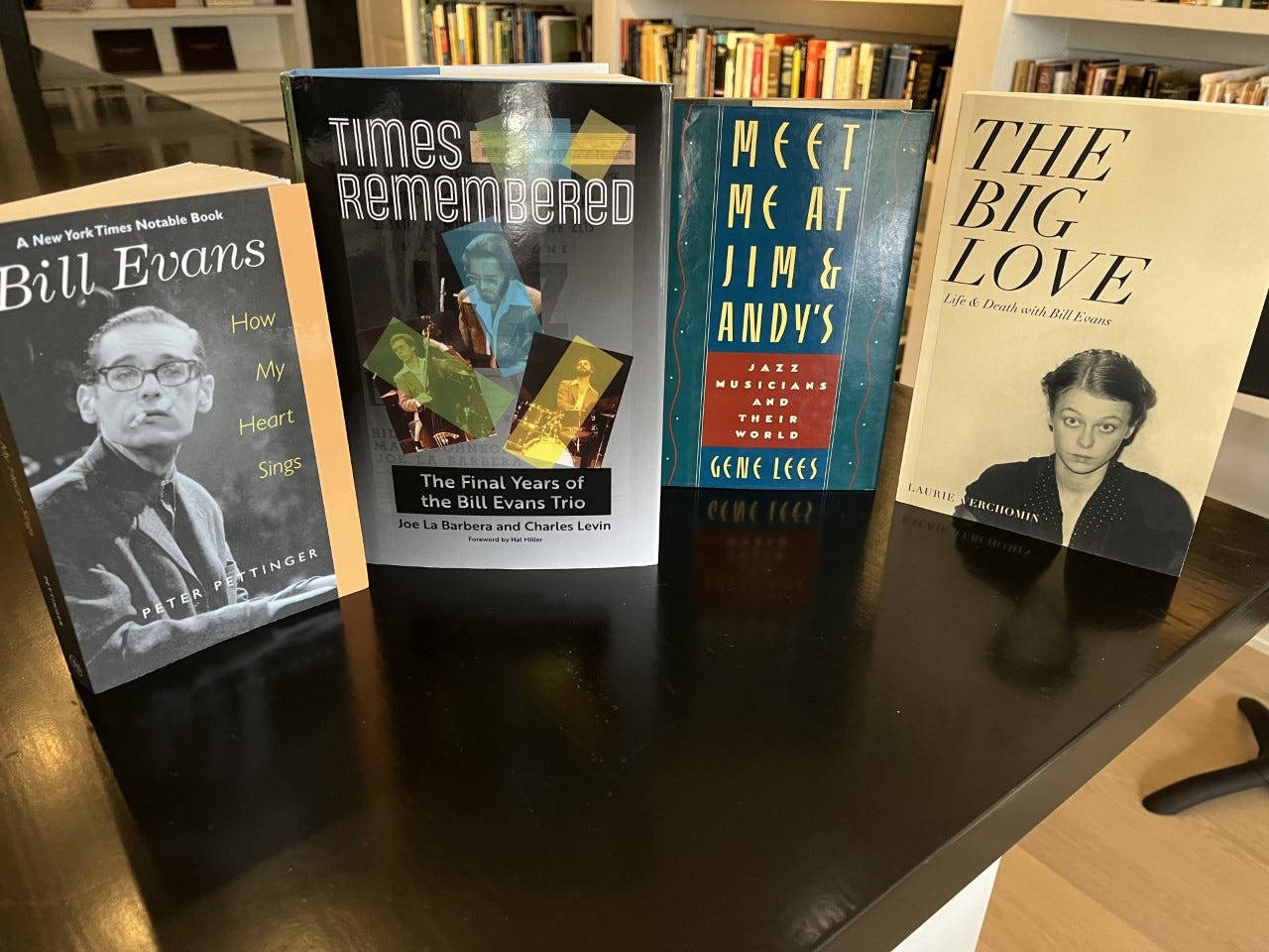 比爾·埃文斯書籍收藏擺放在櫃檯上 壁紙 — 四本關於比爾·埃文斯的爵士傳記書籍放在一張深色木桌上，背景是書架。