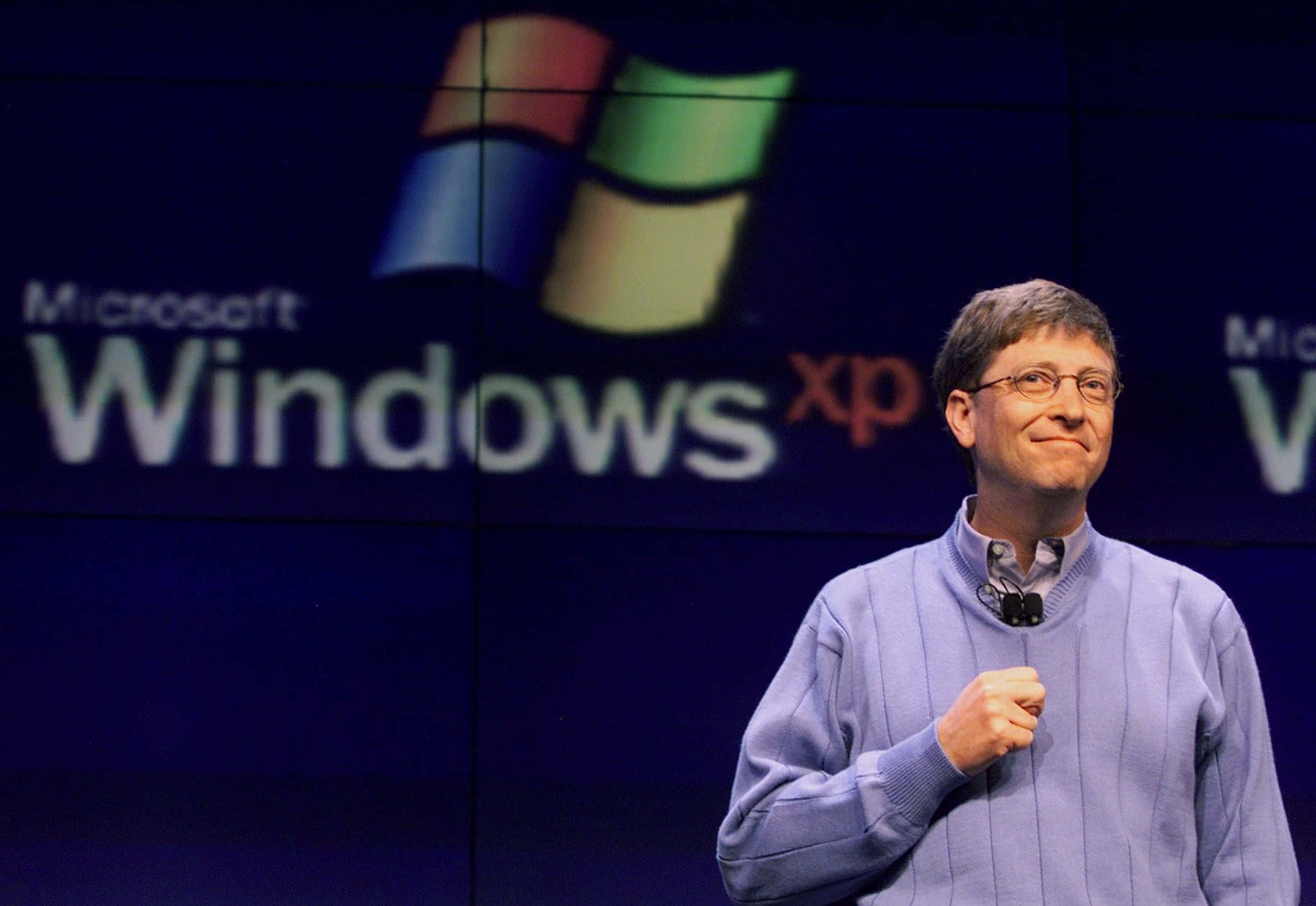 Bill Gates 桌布 壁紙 — 比爾·蓋茨在大型Microsoft Windows XP標誌背景前自信地微笑。