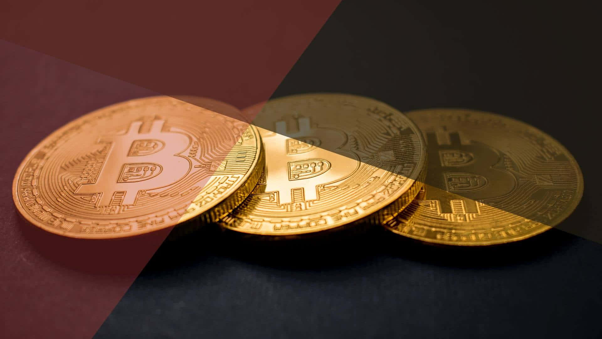 比特幣——今日的密碼學信任貨幣 壁紙 — 三枚閃閃發光的金色比特幣硬幣放置在深紅色和黑色的幾何背景上，帶有戲劇性的燈光。