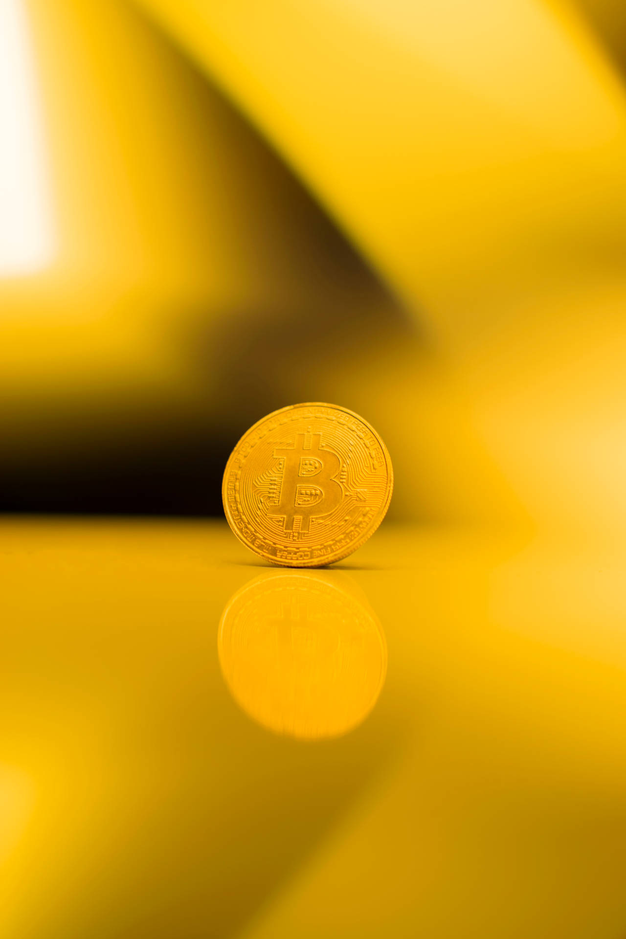金色比特幣硬幣在反射表面上，黃色漸變背景。