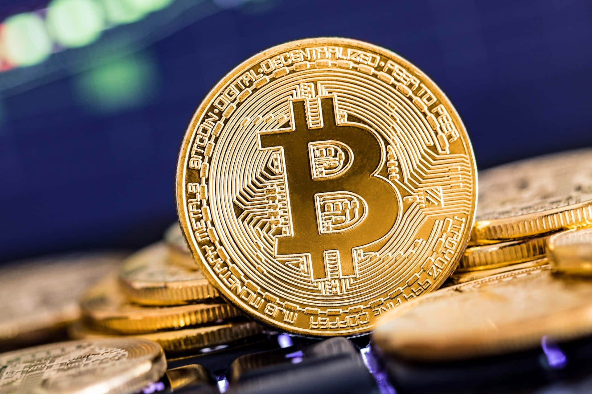 比特幣投資的刺激世界 壁紙 — 一枚閃閃發光的金色比特幣硬幣放在一堆硬幣上，表面蝕刻著電路，背景是模糊的科技背景。