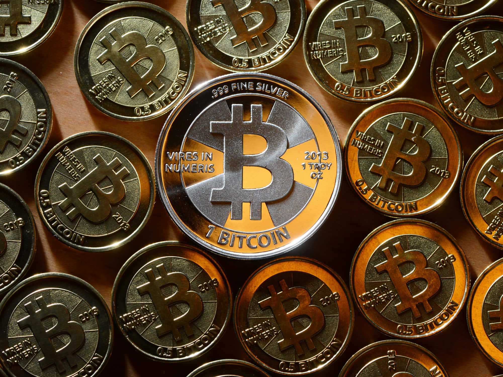 比特幣持續攀升！ 壁紙 — 閃亮銀色和金色比特幣硬幣的特寫，上面刻有「1 BITCOIN」和「0.5 BITCOIN」字樣，以密集圖案排列。