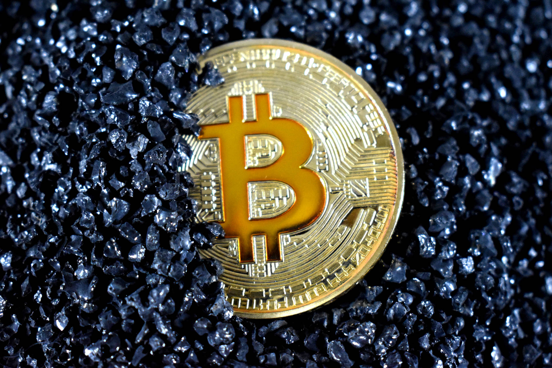 深藍色碎玻璃上的金色比特幣硬幣。