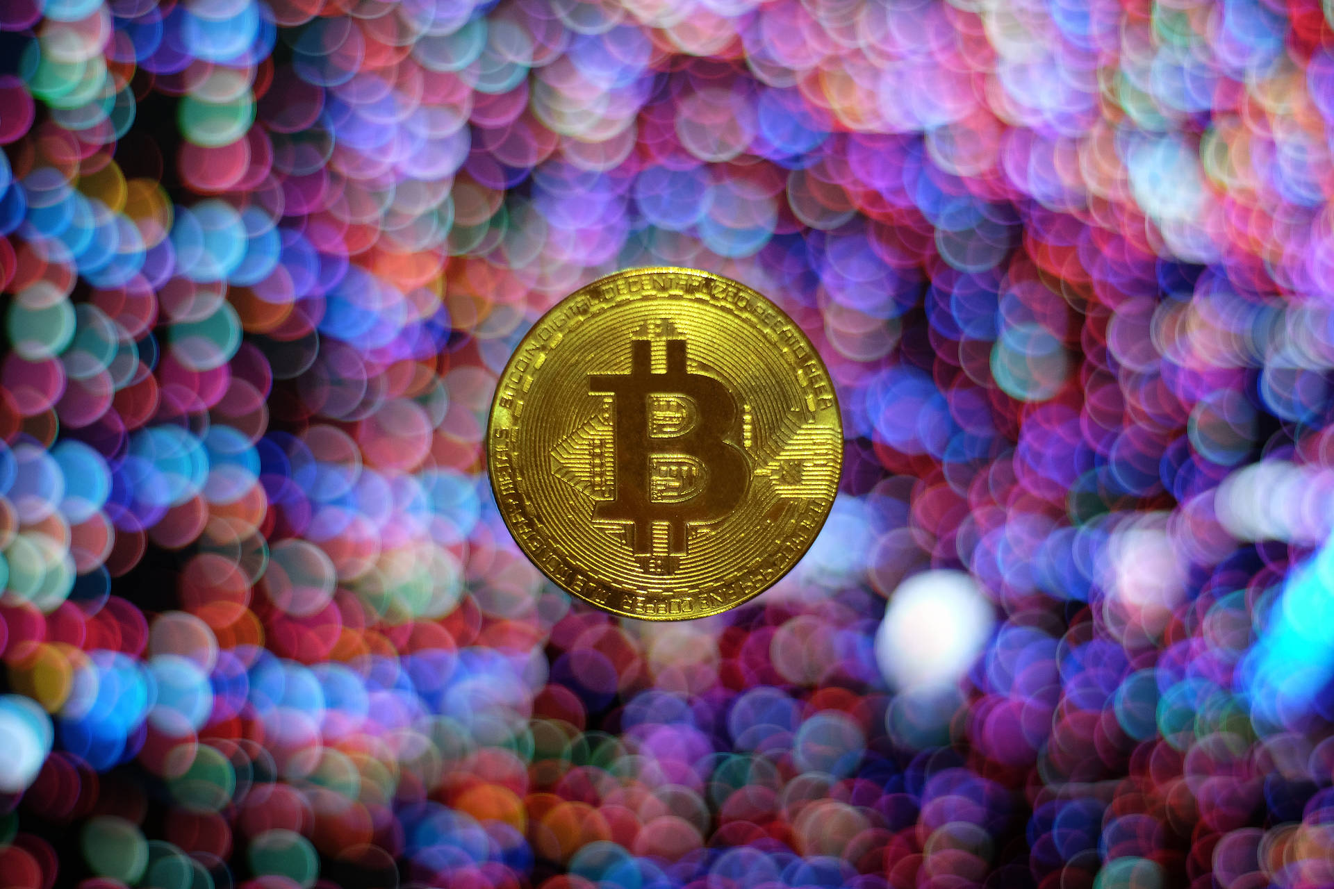 金色比特幣硬幣，背景有彩色模糊燈光