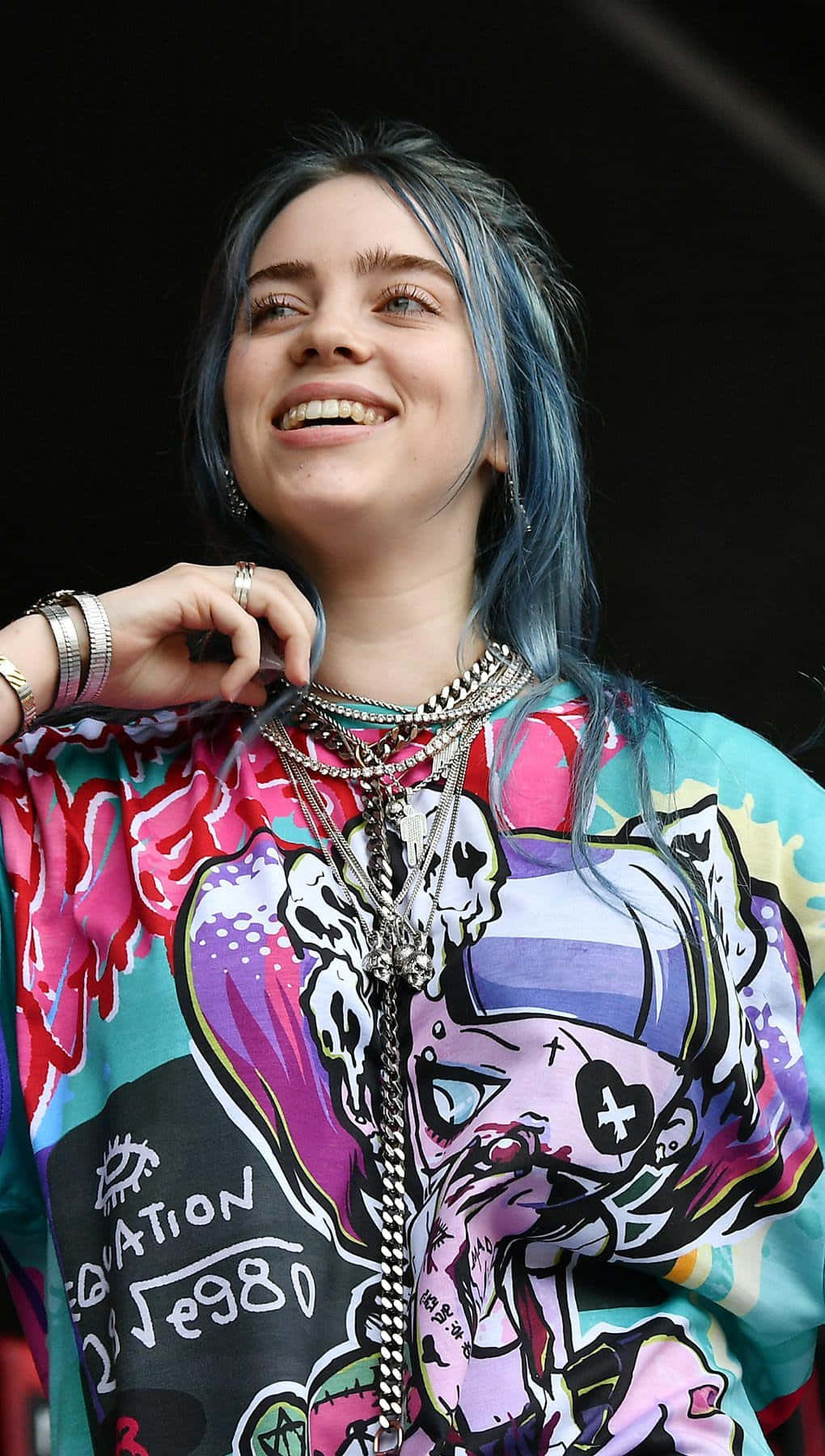 Billie Eilish 在舞台上藍色頭髮配搭層疊珠寶微笑。