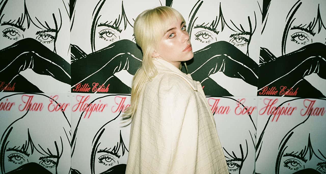 Billie Eilish 身穿米色外套，在她的專輯藝術牆前擺姿勢。