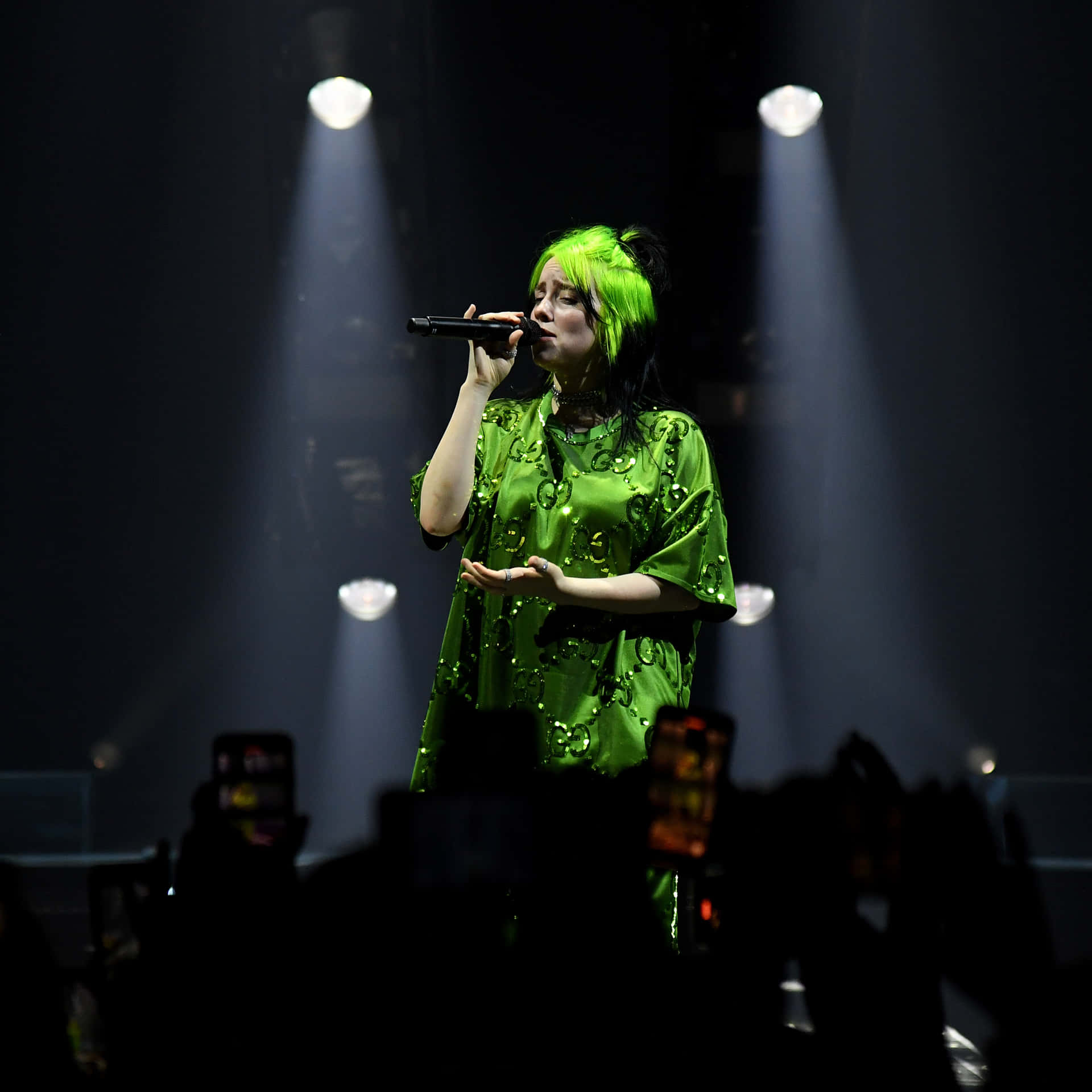 擁有螢光綠色頭髮和服裝的歌手在聚光燈下於舞台上表演。