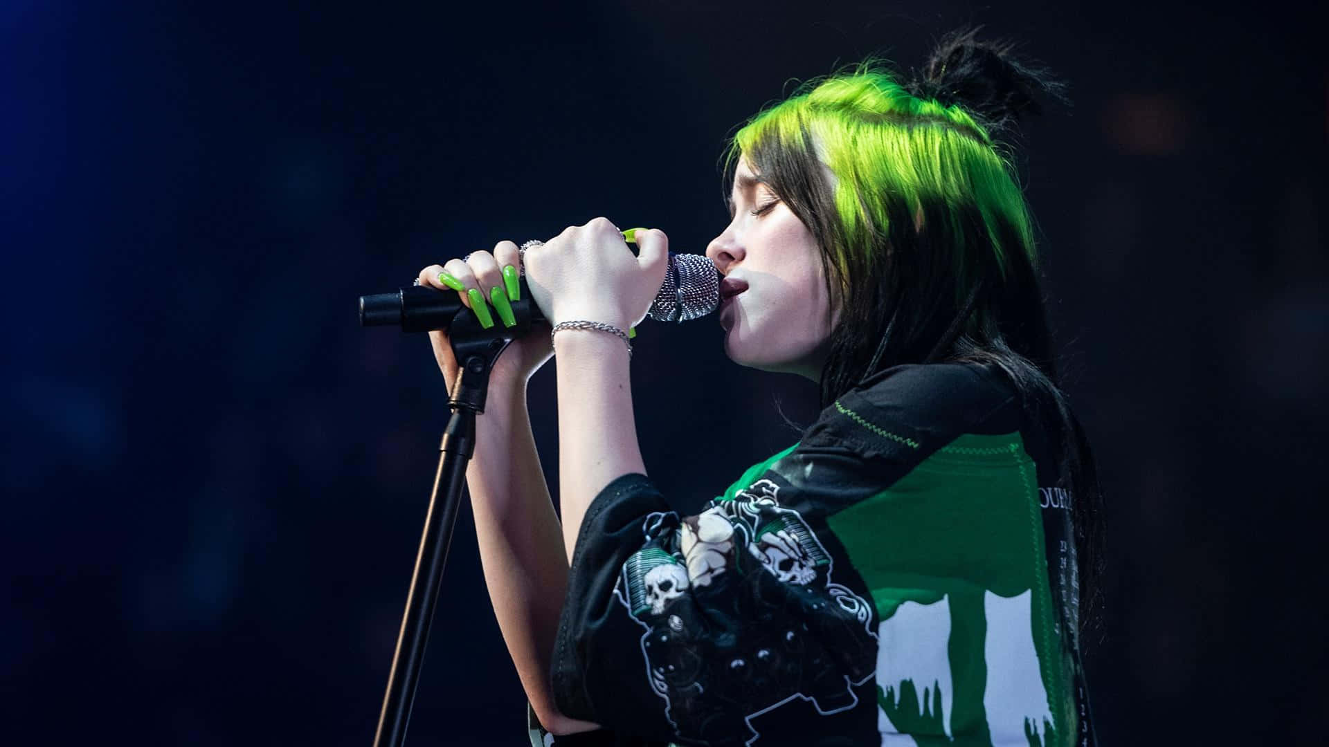 Billie Eilish 在音樂會上留著綠色頭髮對著麥克風唱歌。