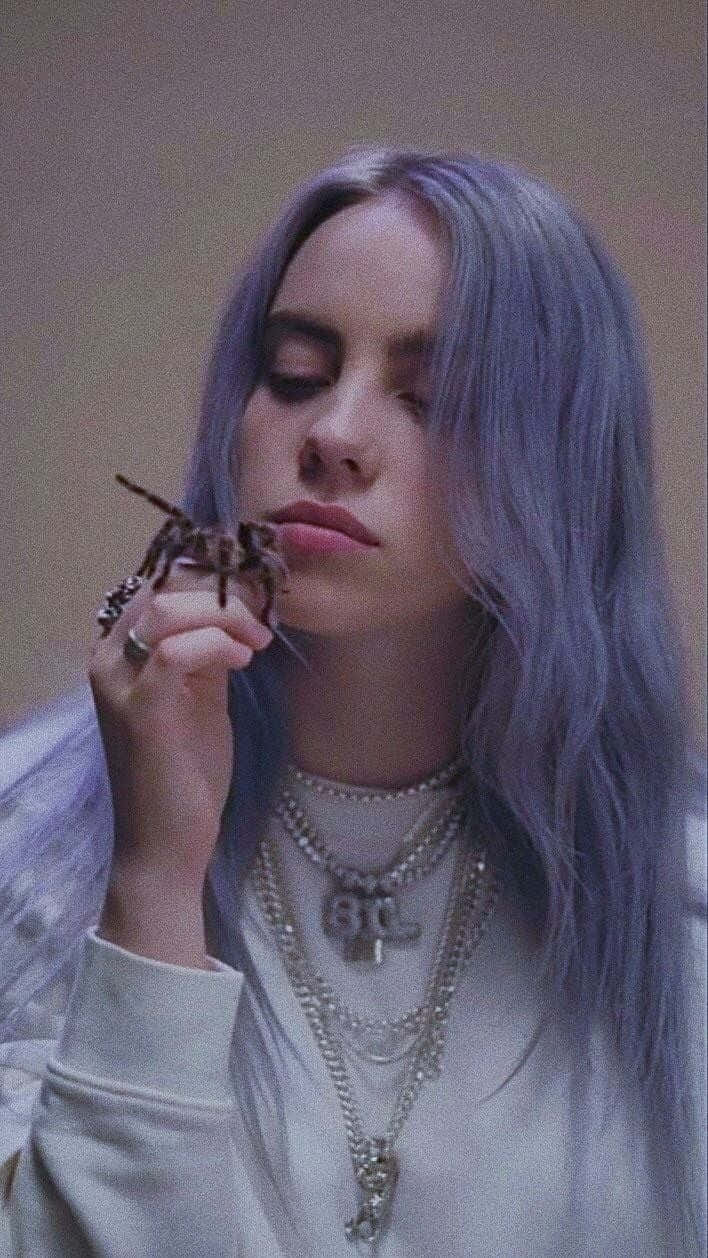 Billie Eilish 拿著狼蛛，紫色頭髮，多層首飾。