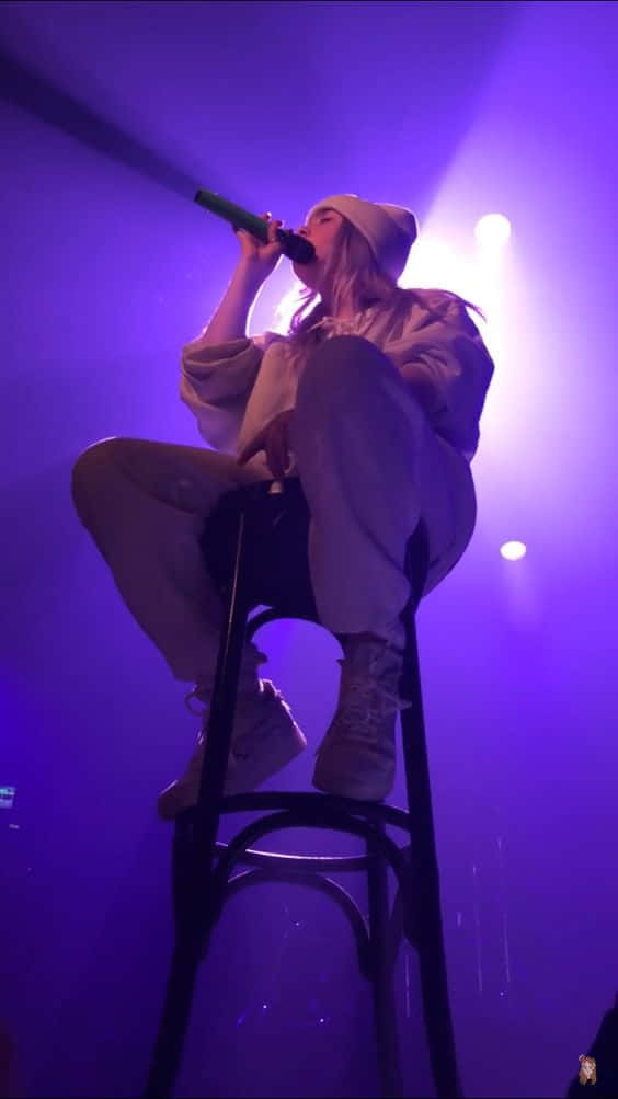 歌手在紫色燈光下坐在凳子上在舞台上表演。