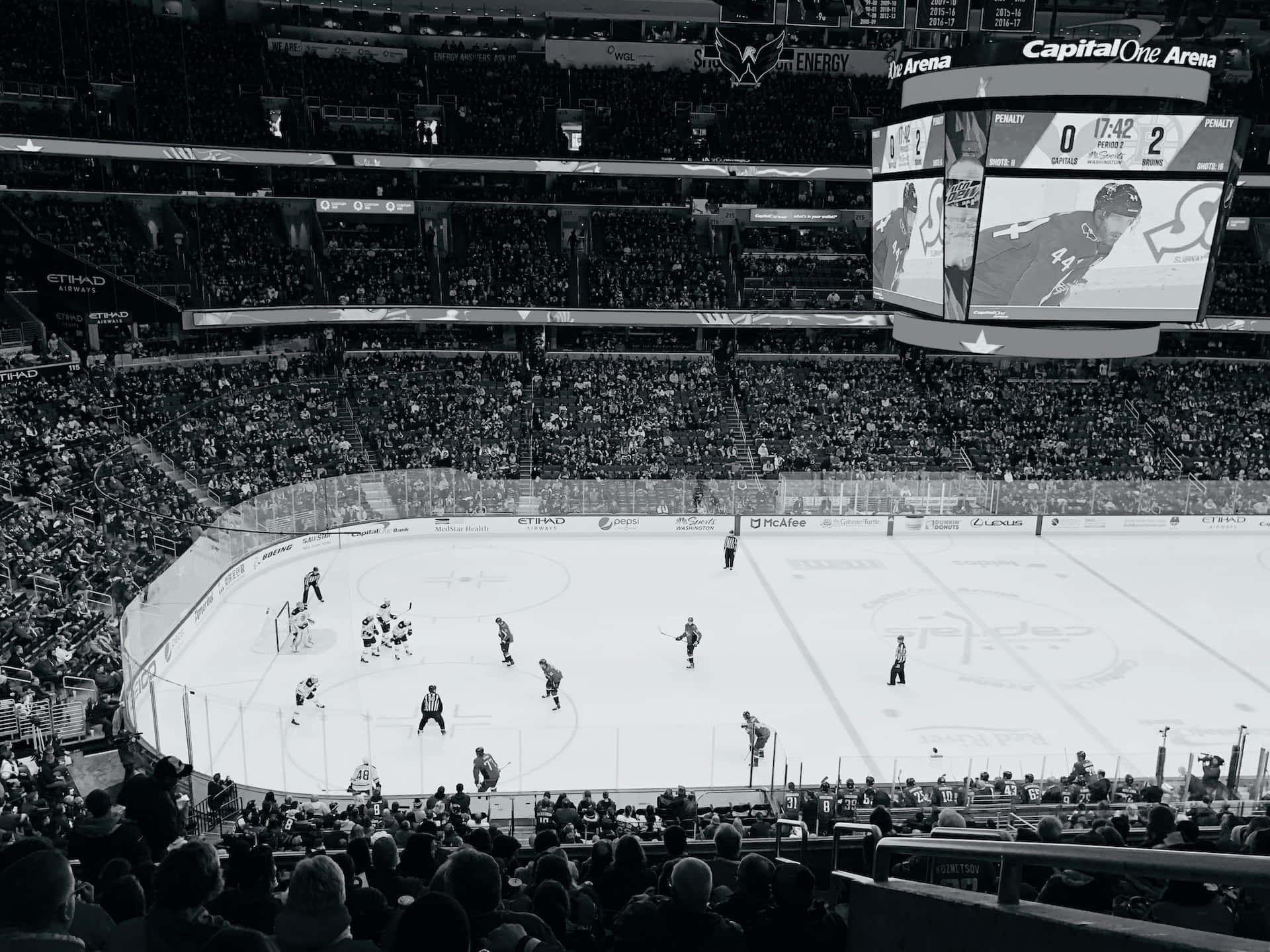 Ice Rink 桌布 壁紙 — 比賽期間，擁擠的冰球場內，球員在冰上，球迷在看台上的黑白照片。