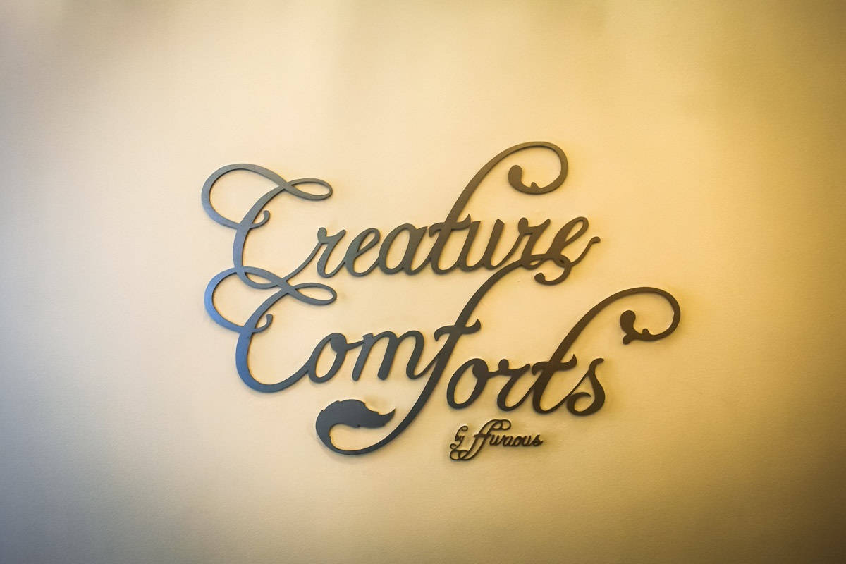 金屬牆藝，上面用優雅的草書寫著「Creature Comforts & Fierce」。