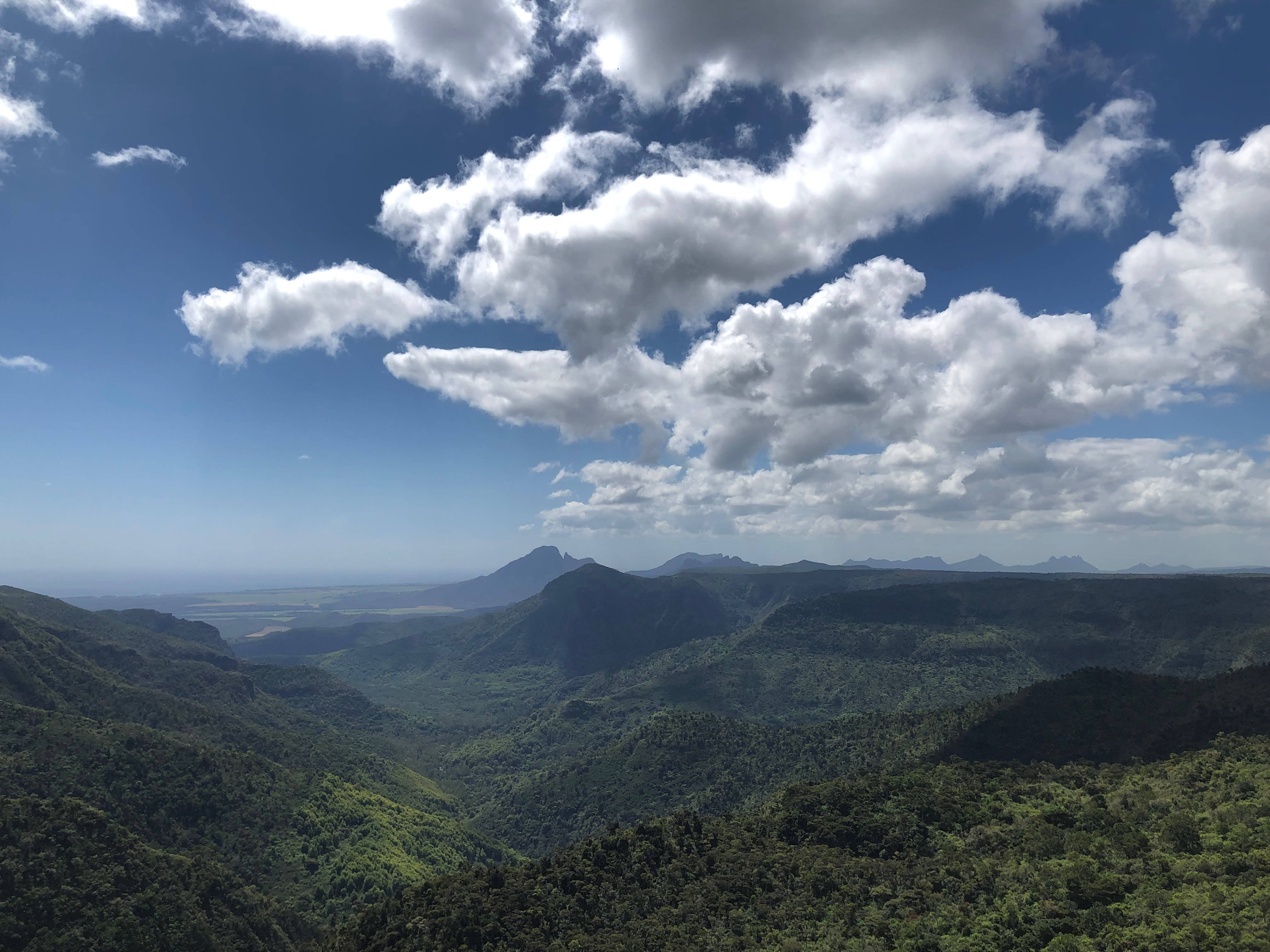 毛里求斯山巒與雲霧 壁紙 — 廣闊的綠色山谷在點綴著蓬鬆白雲的明亮藍天下延伸。