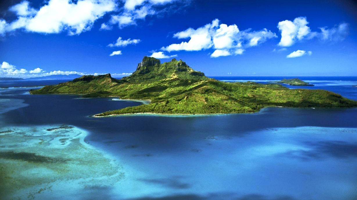 毛里求斯島風景畫 壁紙 — 鳥瞰圖：一個鬱鬱蔥蔥的綠色島嶼，擁有火山峰，被碧綠的潟湖和深藍色的海洋環繞，天空明亮，白雲朵朵。