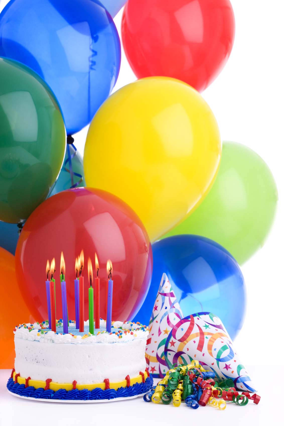 氣球白色生日蛋糕與蠟燭 壁紙 — 一個白色生日蛋糕上插著點燃的蠟燭，周圍環繞著彩色氣球和派對帽，背景為白色。