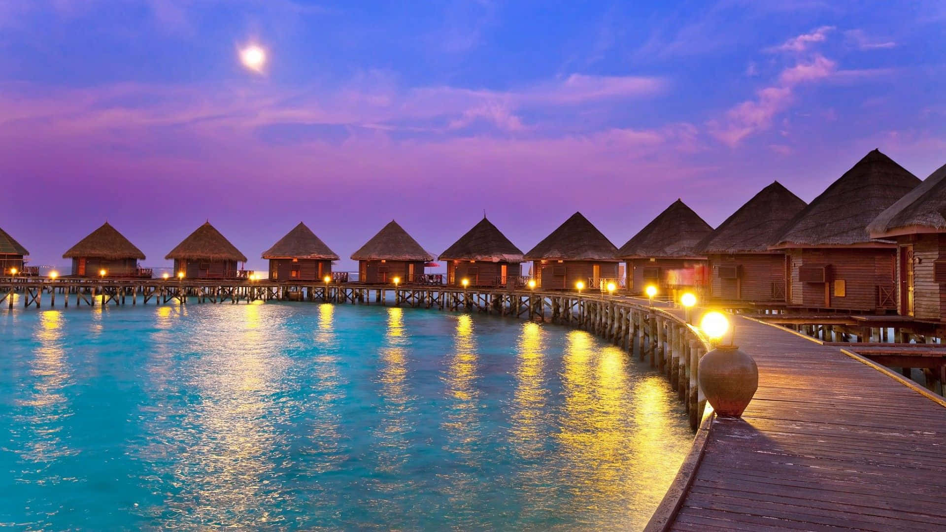 Maldives Beach 桌布 壁紙 — 水上平房在暮色天空下溫暖地發光，明亮的月亮在碧綠的海水上空。