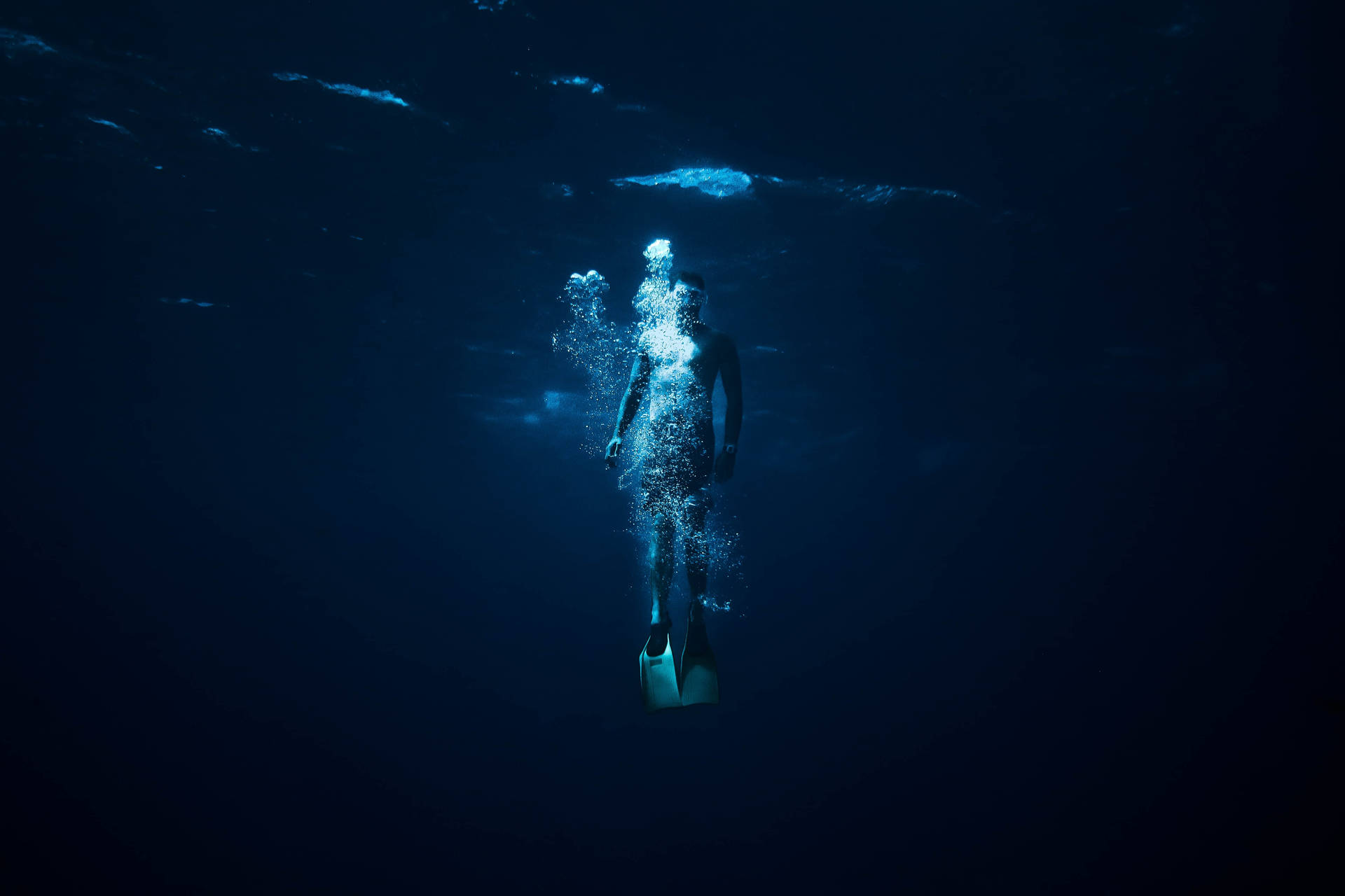一名潛水員在深藍色水中上升釋放氣泡。