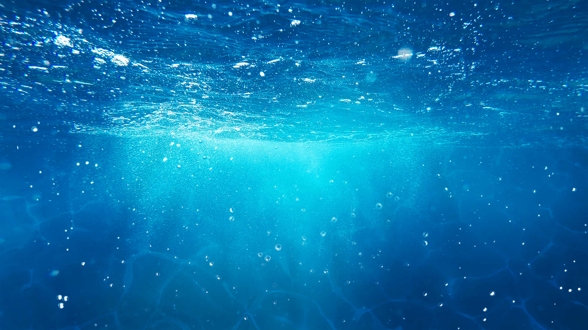 陽光透過清澈的藍色海水，帶有浮動的氣泡和漣漪的水面。