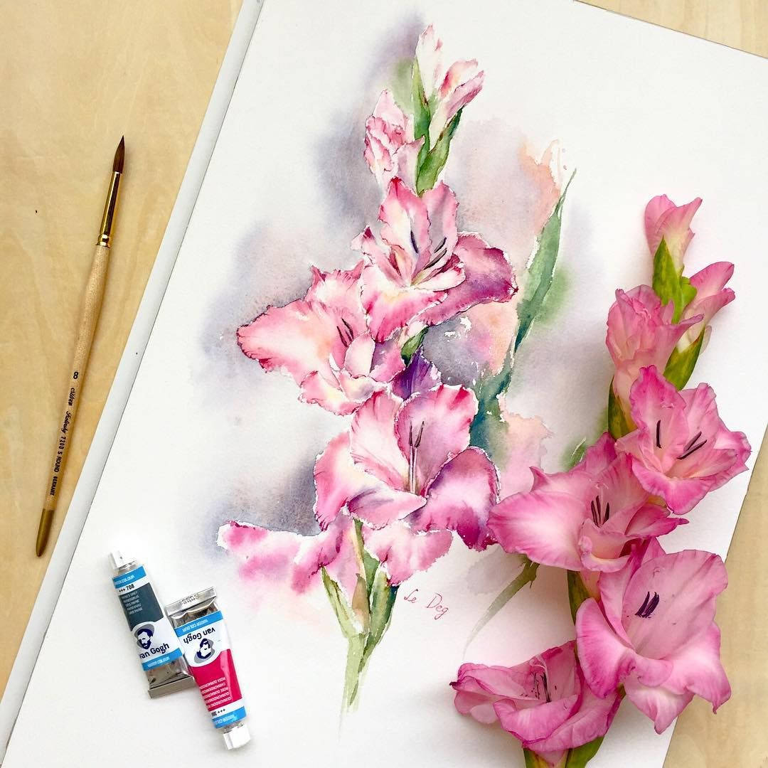 水彩與唐菖蒲花 壁紙 — 一幅水彩畫，描繪白色紙上的粉紅色劍蘭花，旁邊有顏料管和畫筆放在木質表面上。