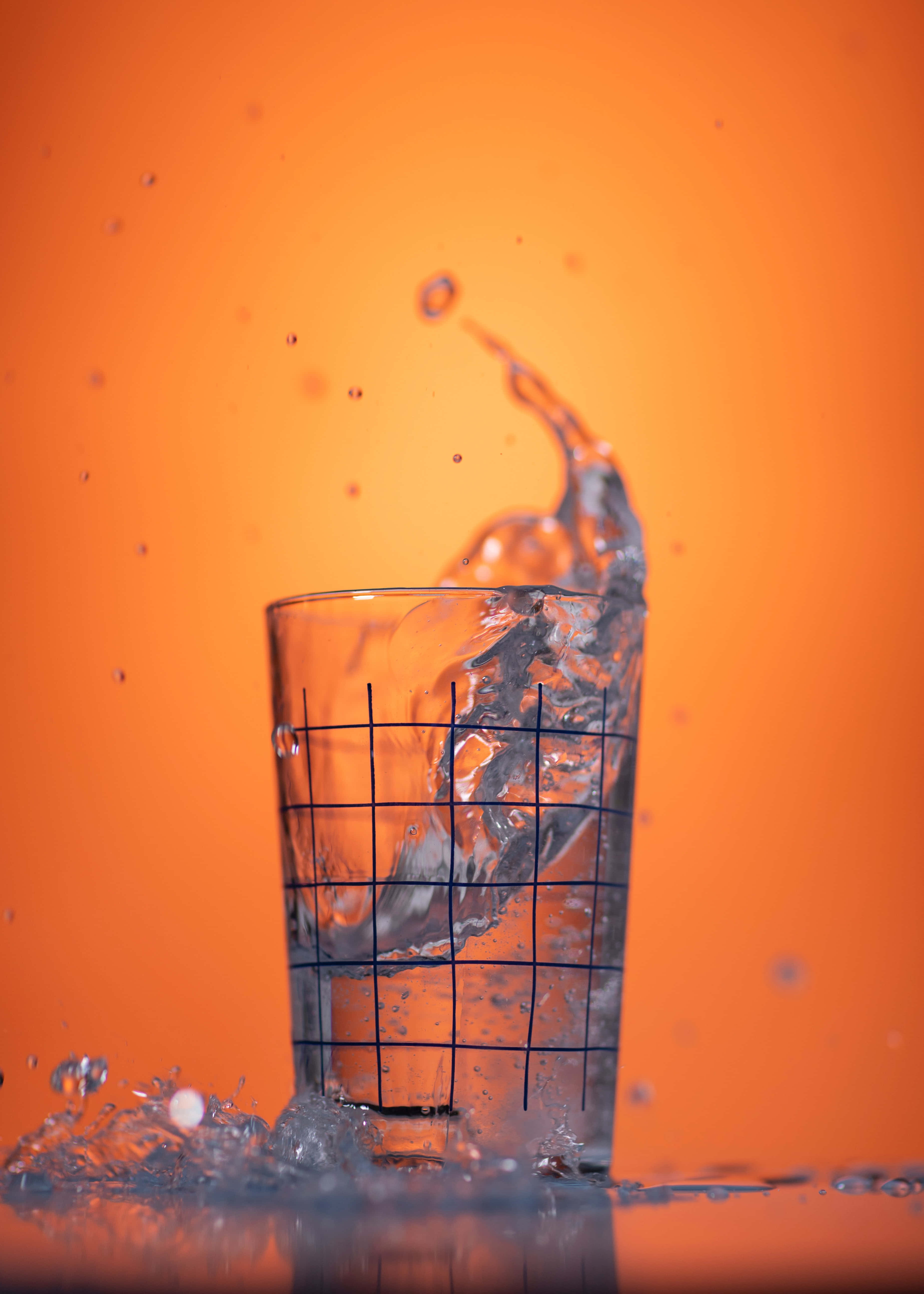 Hydration 桌布 壁紙 — 水從玻璃杯中噴出，在充滿活力的橙色背景上形成動態水花。