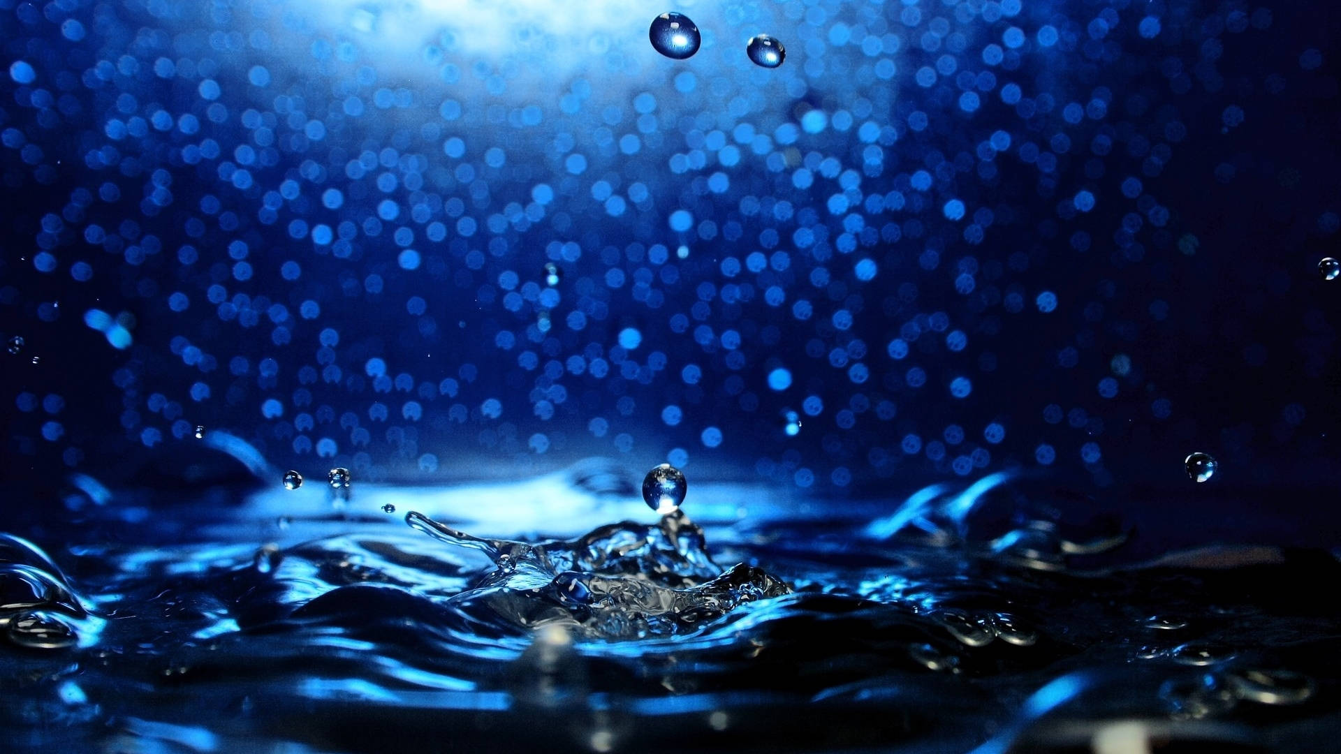 水下 桌布 壁紙 — 水滴懸浮在漣漪藍色表面上空的特寫，背景有散景效果。