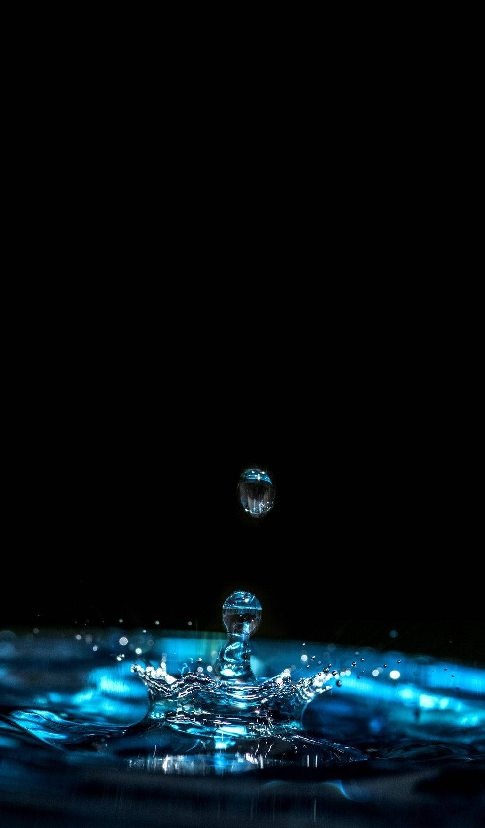 懸浮的水滴即將擊中藍色液體表面，背景為黑色。