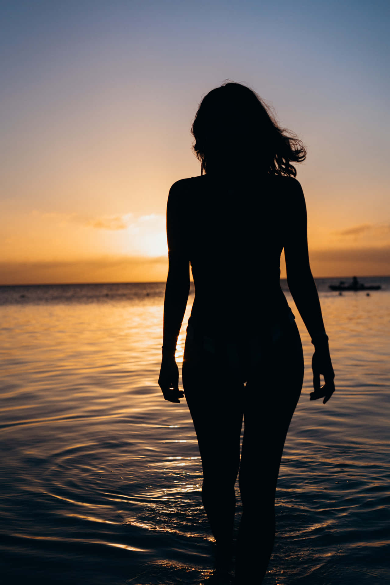 女性在金色日落時分於海水中行走