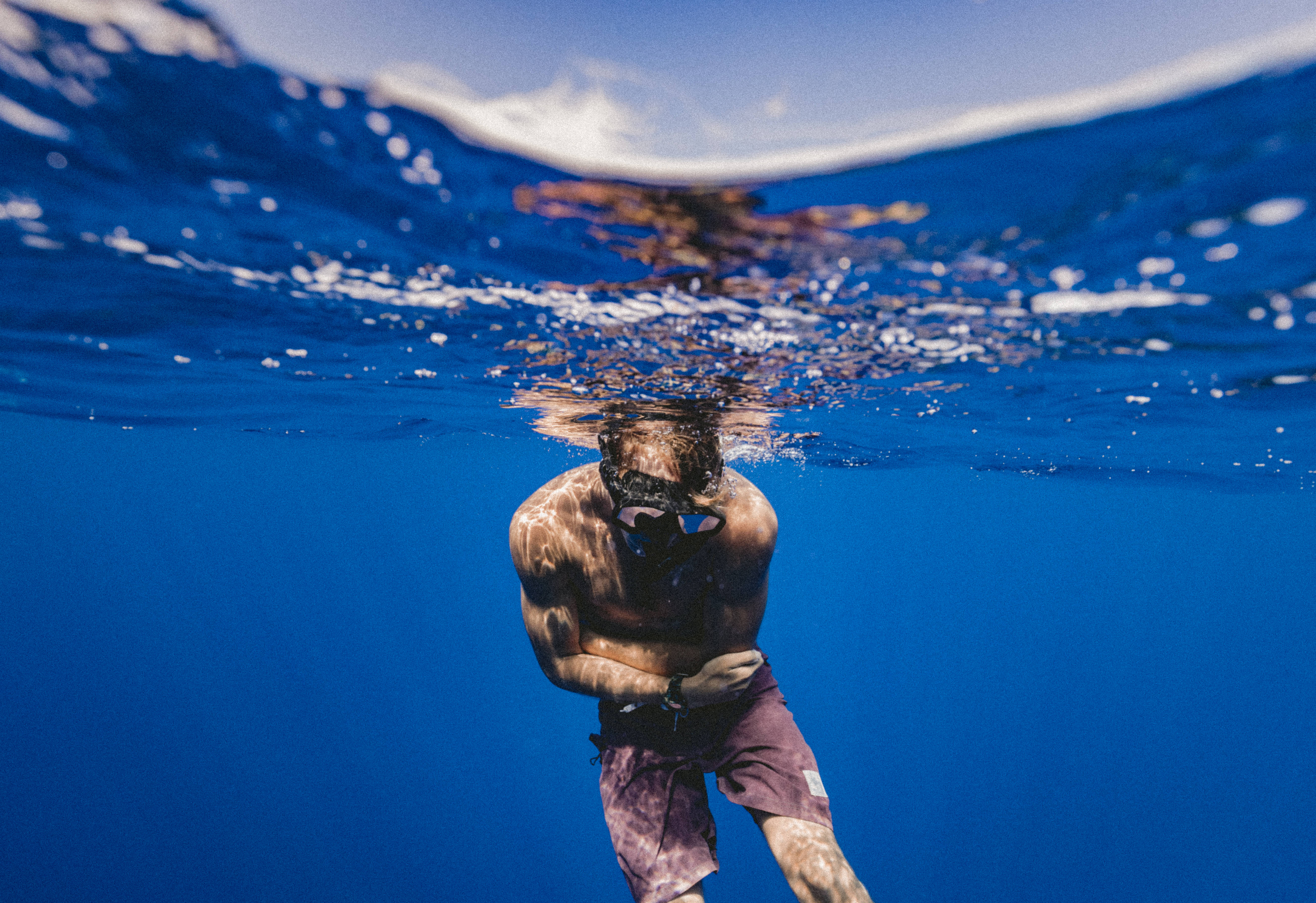 水面線浮潛特寫 壁紙 — 一名浮潛者在水晶般清澈的藍色海洋中於水下滑行，陽光從上方水面過濾而下。