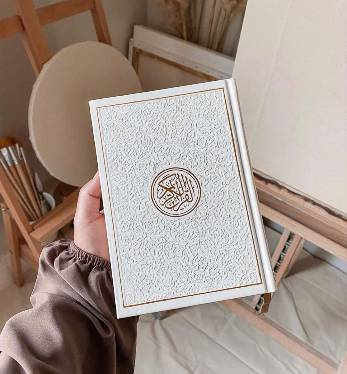 在米色藝術工作室中，手拿著一本白色壓花古蘭經。