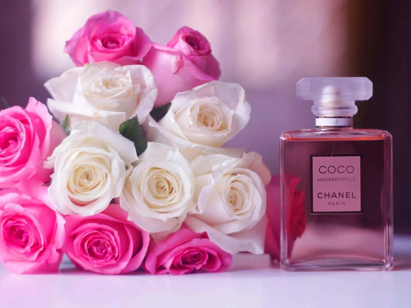 永恆奢華——香奈兒經典風貌 壁紙 — 一瓶 Chanel Coco Mademoiselle 香水放在一束柔焦的粉紅和白色玫瑰旁邊。