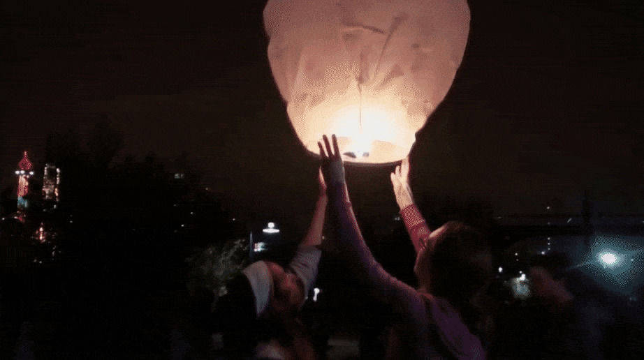 永遠的好朋友紙燈籠 壁紙 — 兩個人在遠處城市景觀上方的黑暗夜空中釋放一個發光的天燈。