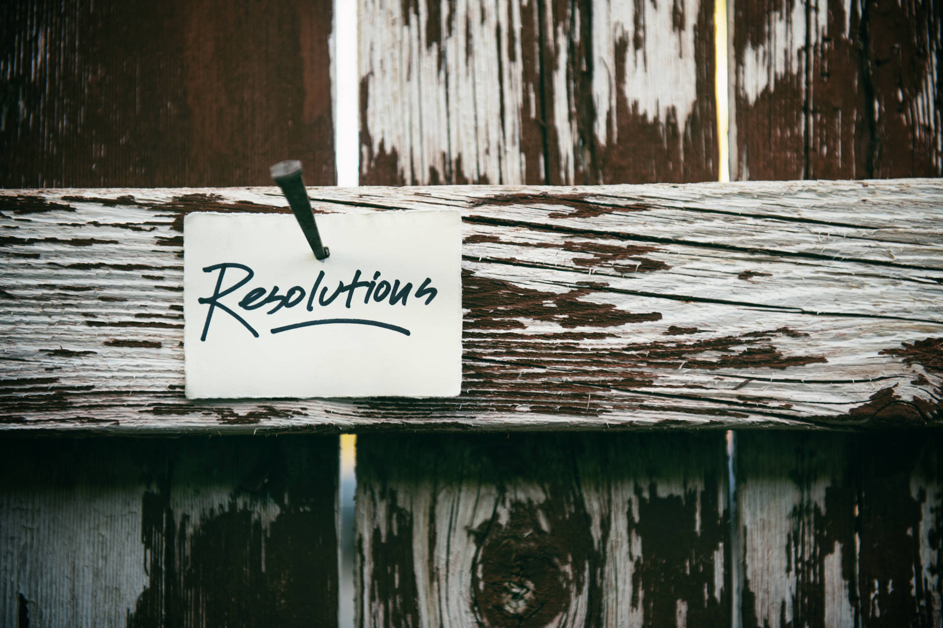 手寫便條釘在風化木柵欄上，寫著Resolutions。