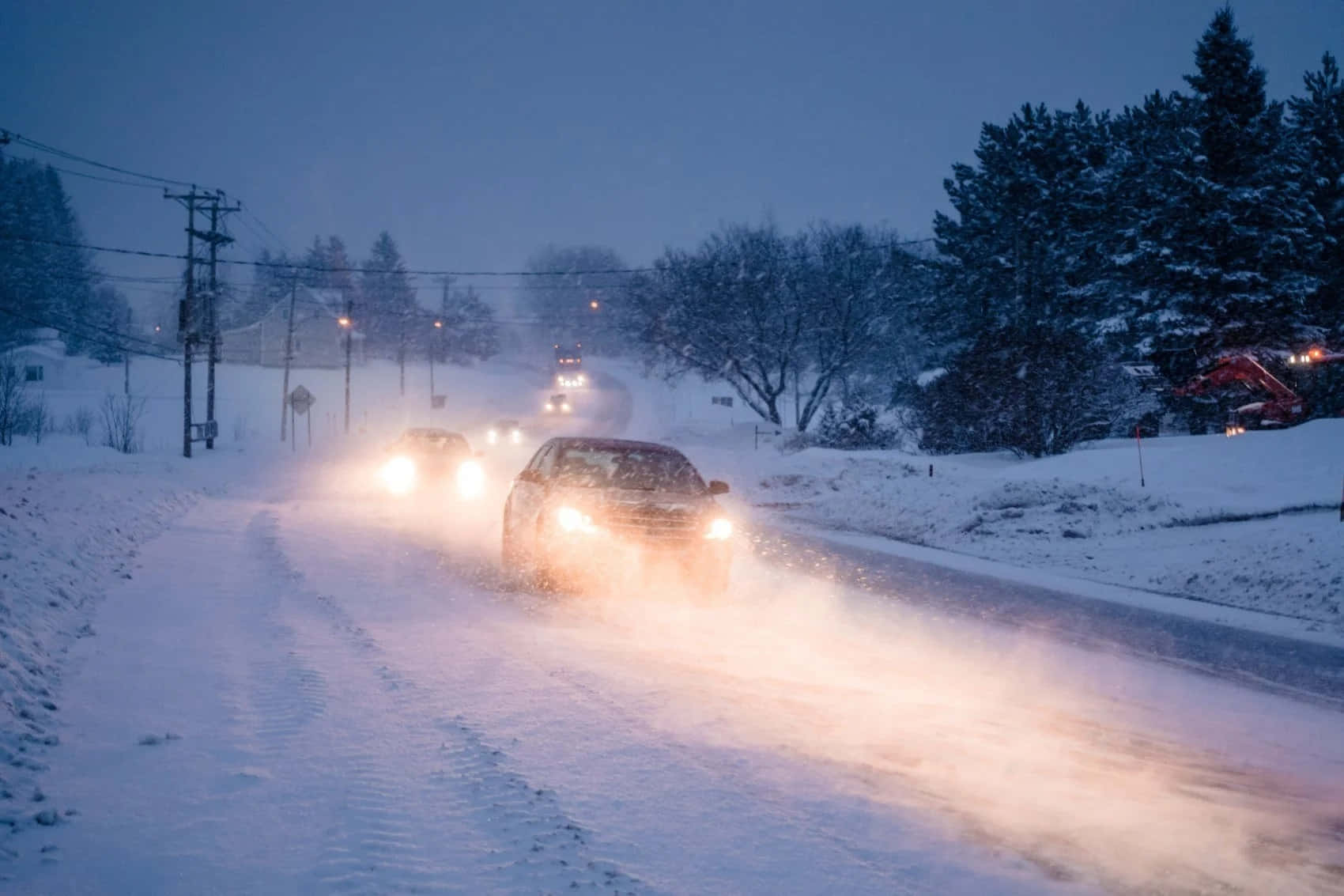 Winter Driving 桌布 壁紙 — 汽車亮著明亮的車頭燈，在寧靜的冬季道路上，穿過厚厚的積雪，道路兩旁是積雪的樹木和電線桿，天空暮色蒼茫。