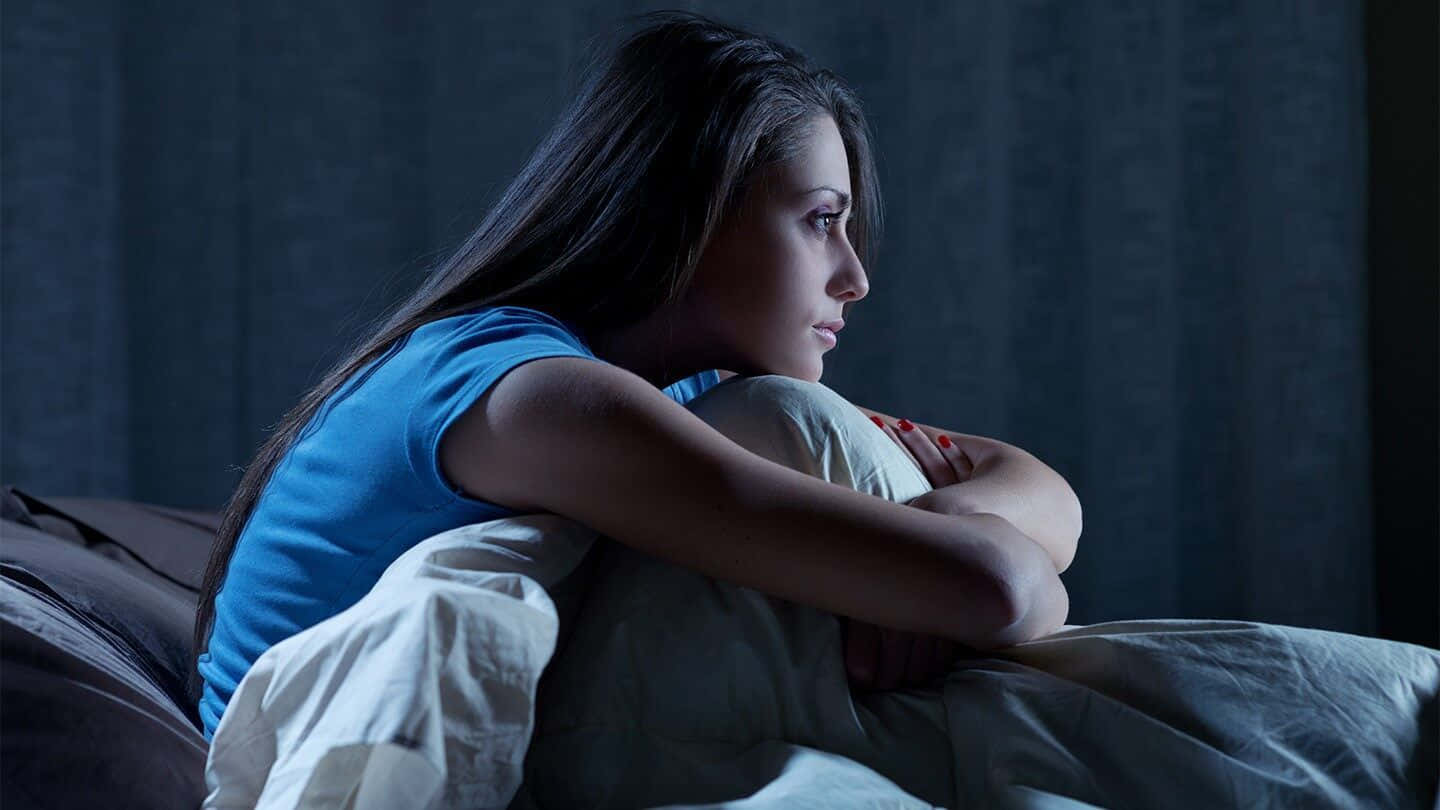 一位年輕女性夜晚獨自坐在床上，若有所思。