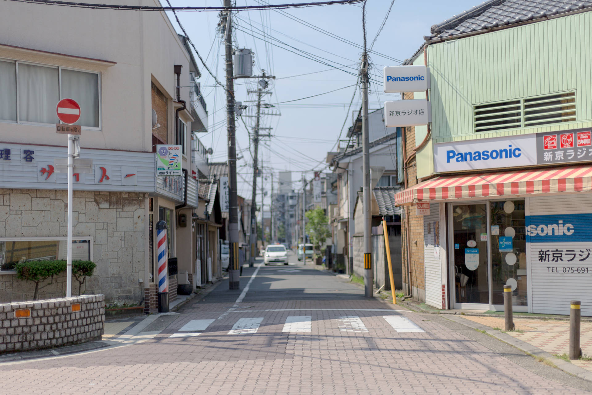 一條寧靜的日本城市街道，有商店和電線，天空晴朗。