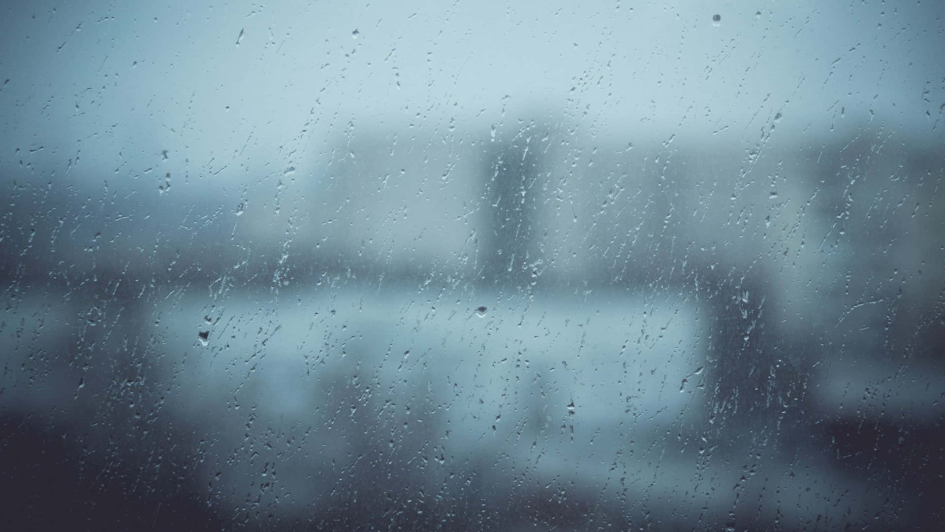 窗上的雨滴，藍色調的模糊城市景觀。
