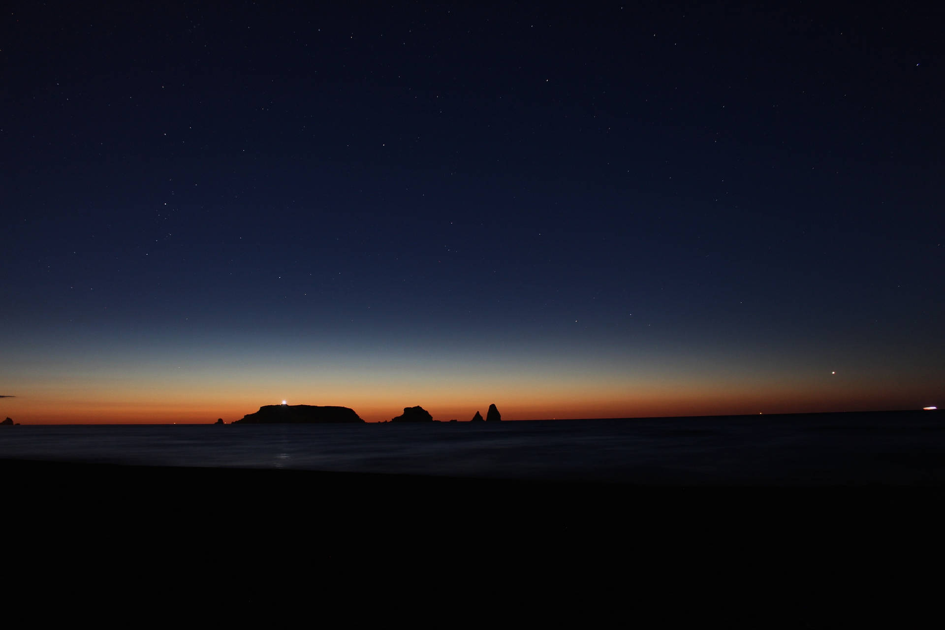 夜晚的黑暗海灘，星空和海洋岩石上發光的地平線。