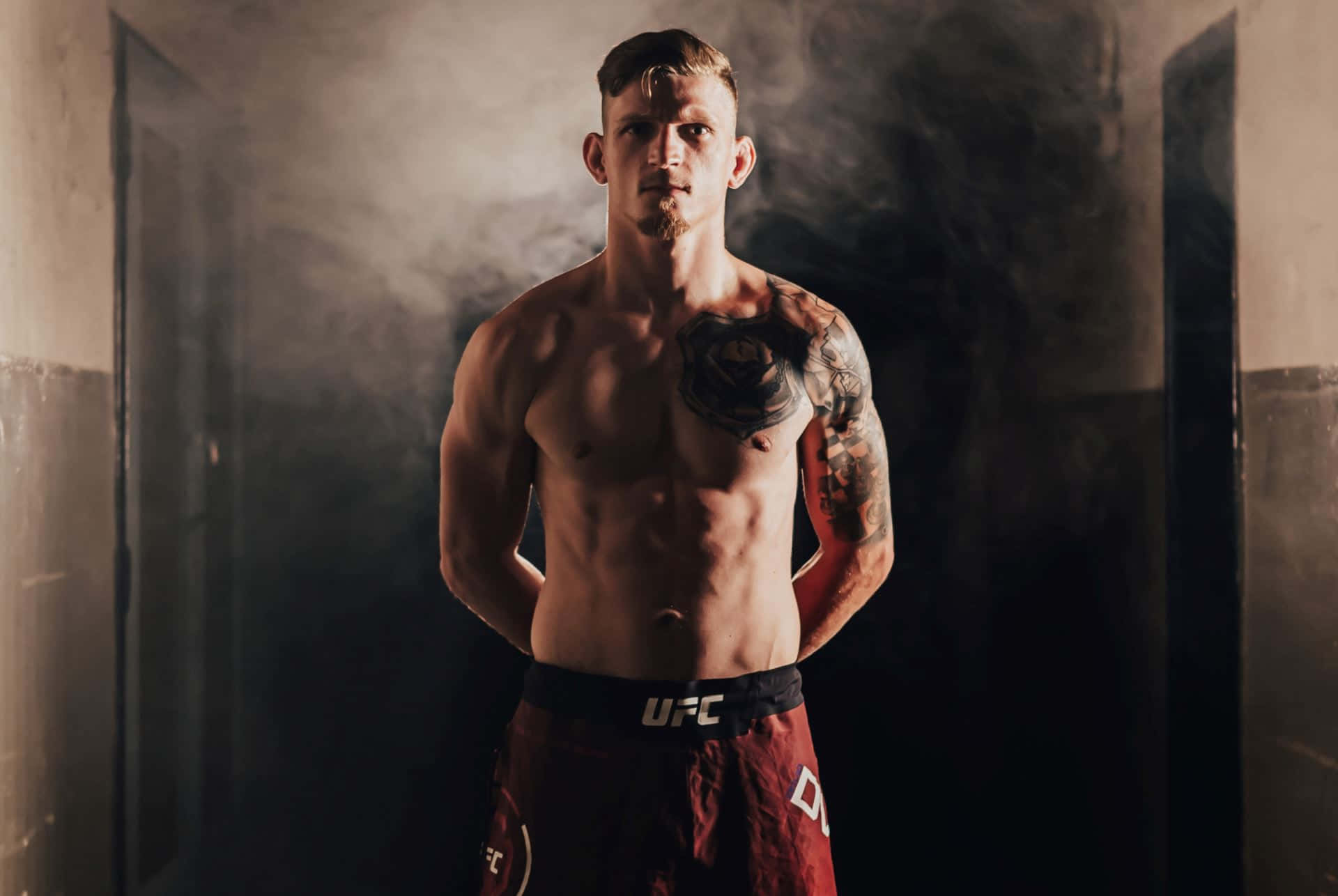 一位赤裸上身、帶有紋身的男性UFC拳手站在煙霧瀰漫的走廊中。
