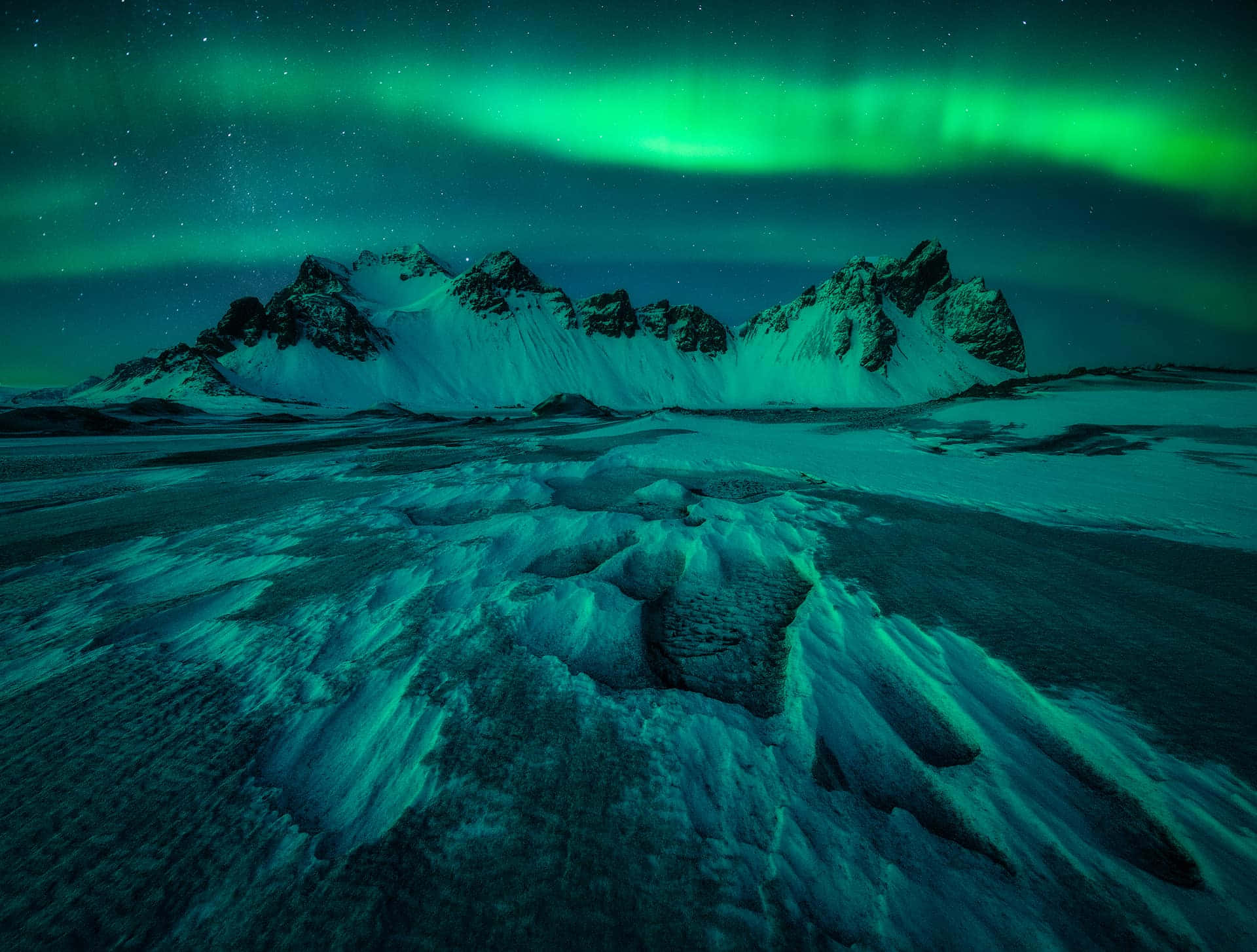 綠色北極光在星空下，照亮積雪的山脈和冰凍的地面。